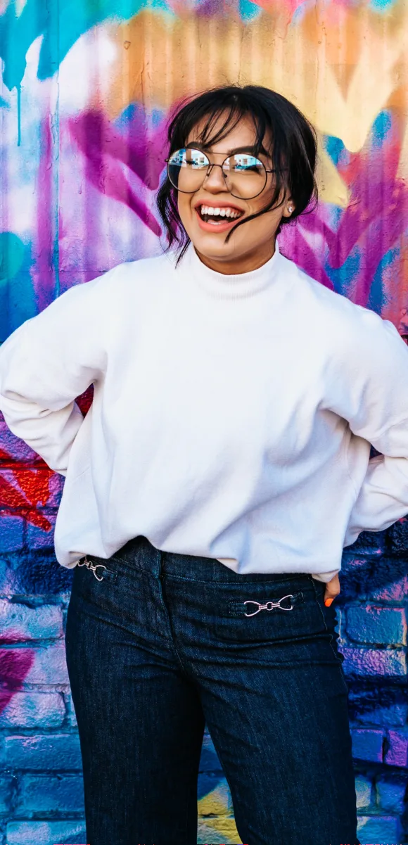 A woman smiling in front of a colorful mural